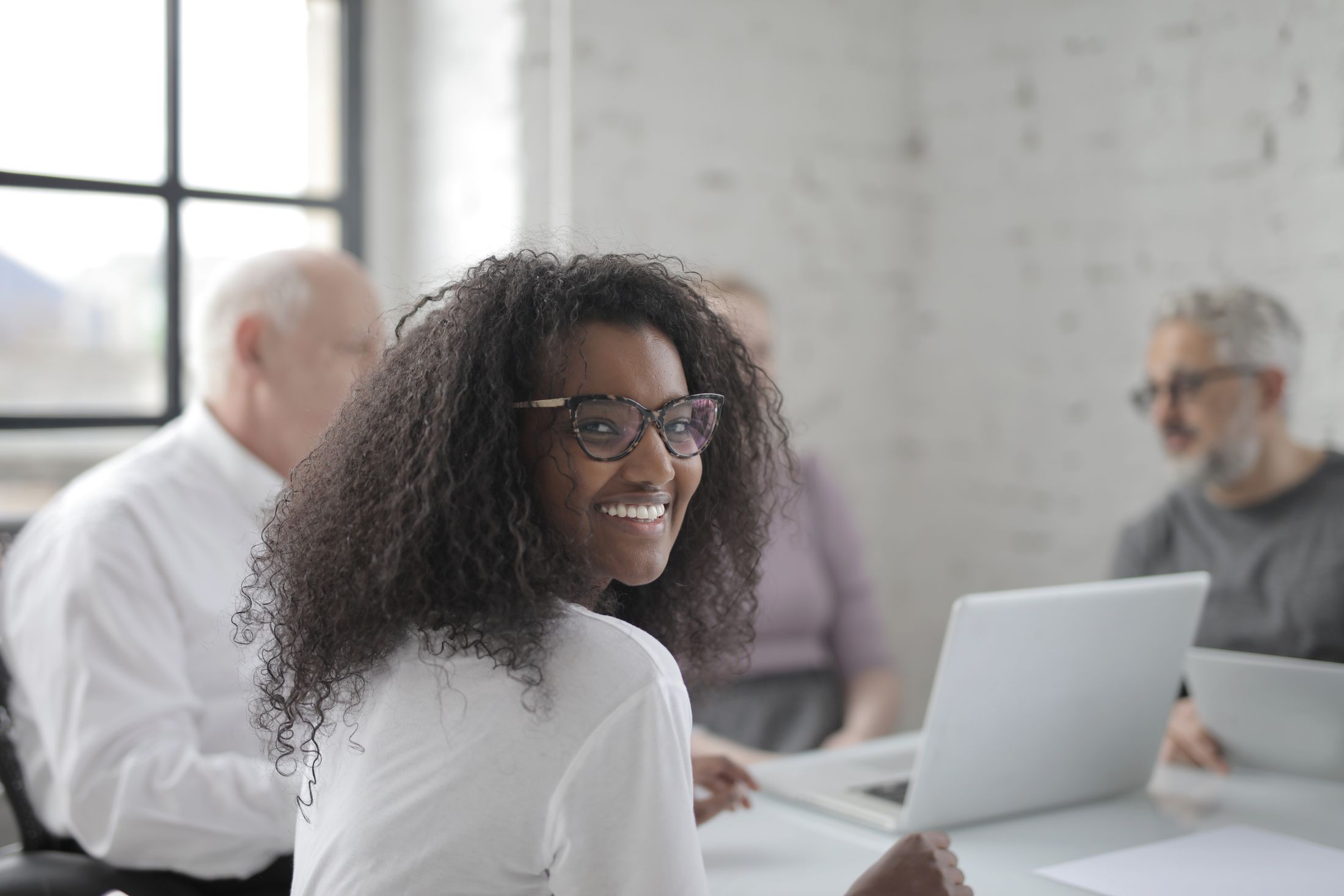 A smiling professional at her laptop, with experienced colleagues working together in a bright office